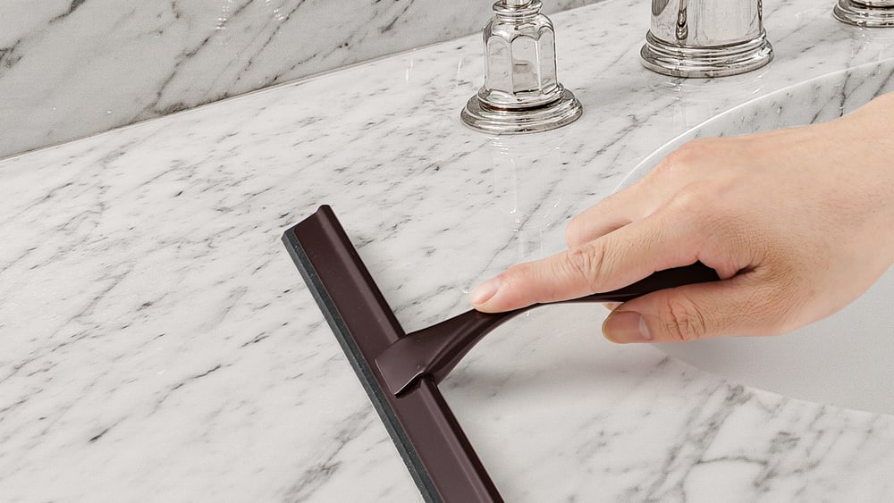 A hand drawing a squeegee down a wet shower screen